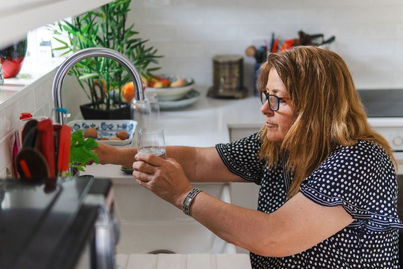 Une femme remplit un verre d’eau dans sa cuisine