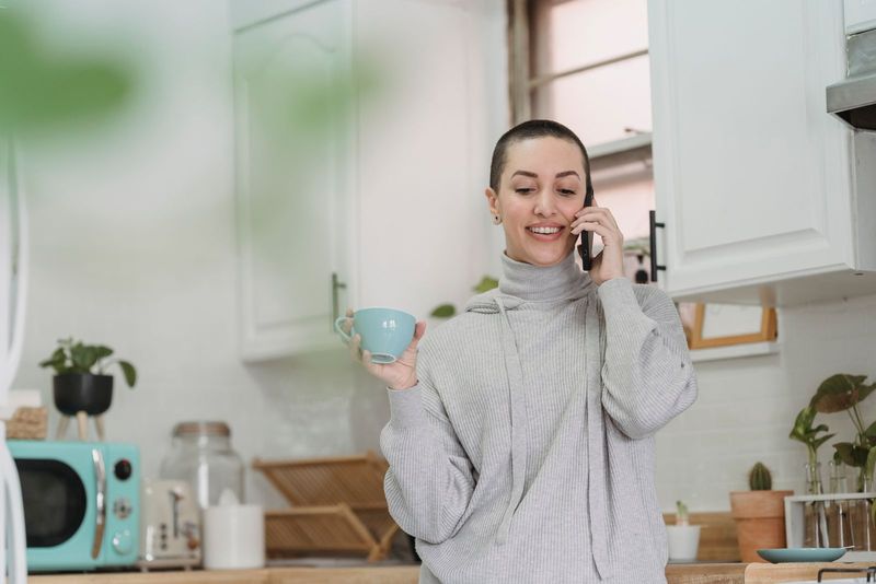 Une jeune femme prend un café dans sa cuisine, le téléphone à l’oreille